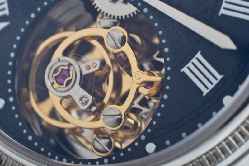 Close-up of a modern tourbillon carriage turning in an opening in a dark blue dial